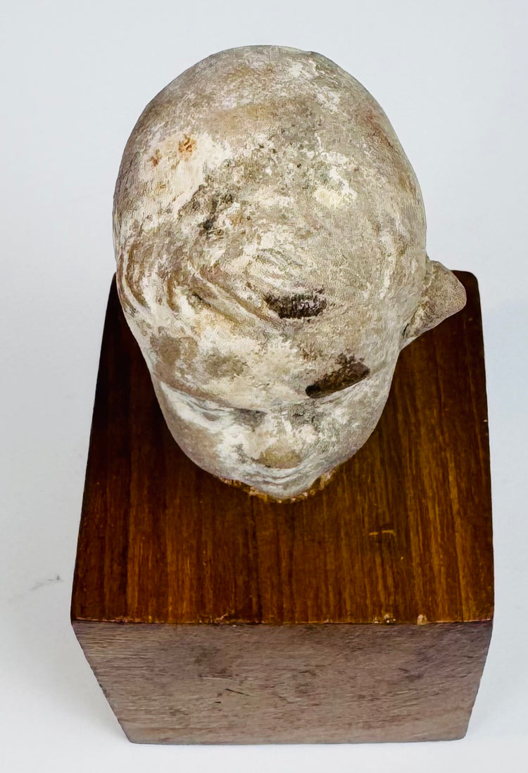 Terracotta head fragment highlighting swept hair grooves and pale surface wear across the rounded crown and forehead.