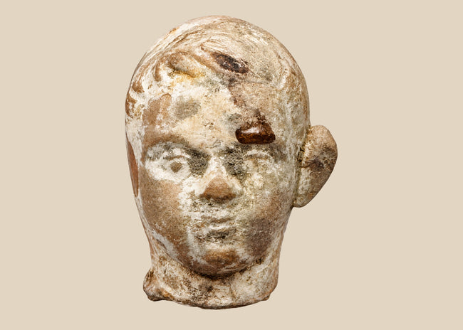 Video of an ancient terracotta head fragment on a wooden base, showing youthful facial features, sculpted hair, and a weathered surface.