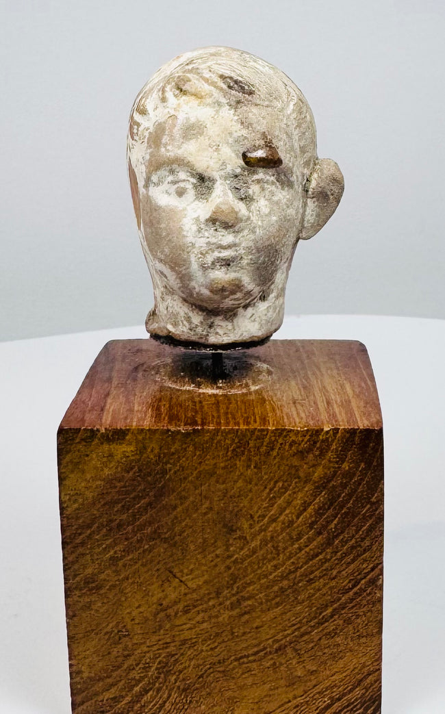 Ancient terracotta head displaying rounded cheeks, defined brows, and a prominent ear above a square wooden display base.