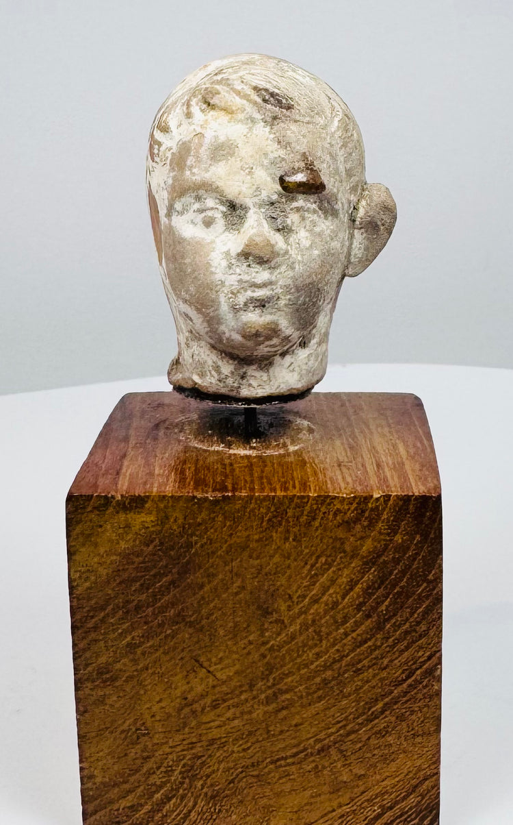 Ancient terracotta head displaying rounded cheeks, defined brows, and a prominent ear above a square wooden display base.