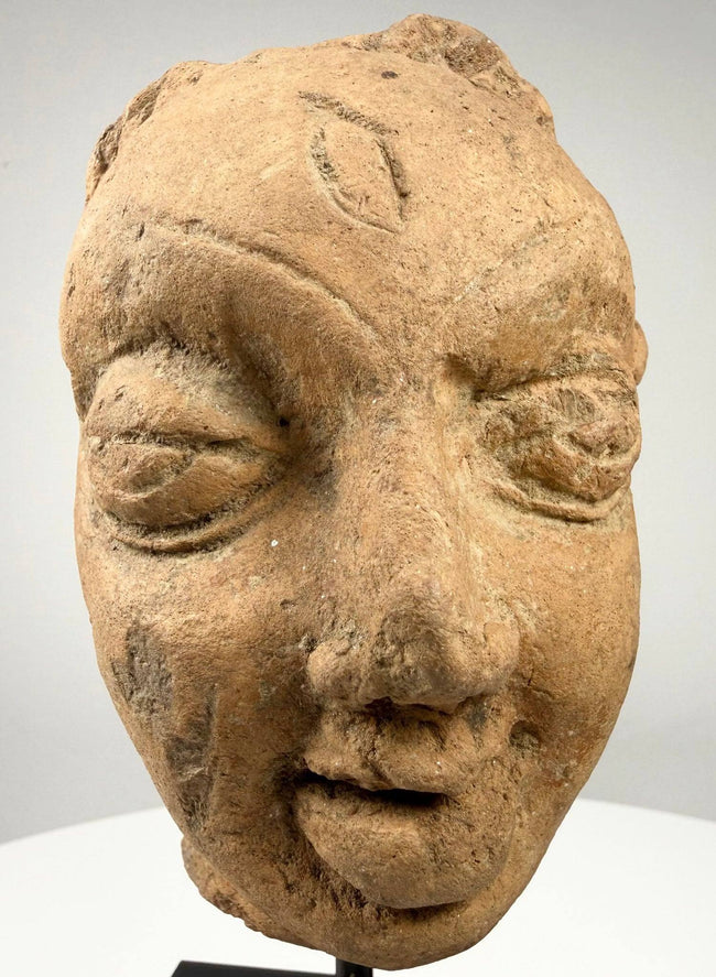 Frontal close-up of ancient Indian terracotta sculpture head with bindi mark and serene expression