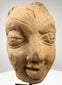 Frontal close-up of ancient Indian terracotta sculpture head with bindi mark and serene expression