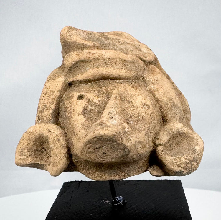 Ancient Mesoamerican stone head with elaborate headdress and weathered tan surface