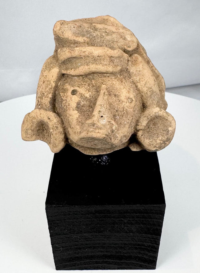 Ancient Mexican stone head with large ear ornaments and stylized facial features