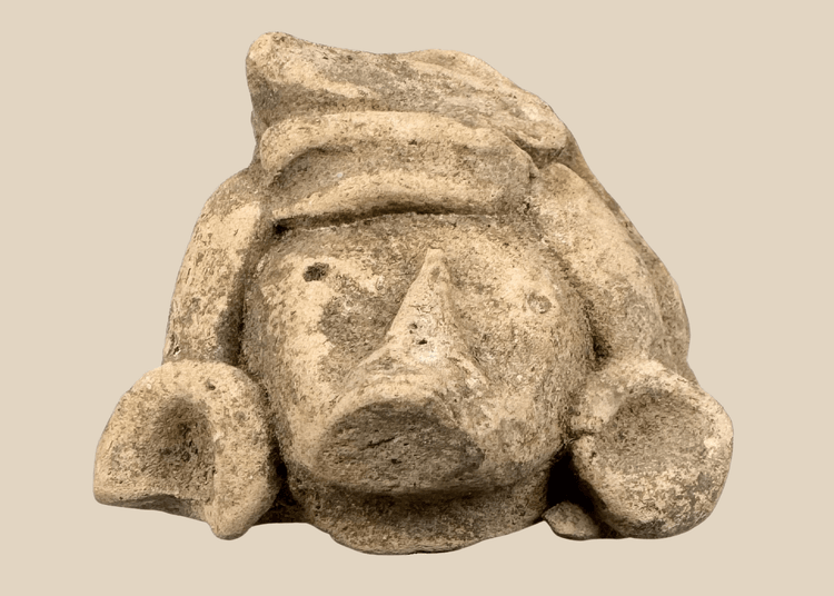 Pre-Columbian carved stone head fragment with recessed eyes, triangular nose, and circular earspools
