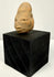 Antique terracotta head sculpture placed on black cubic block to showcase artifact size and form