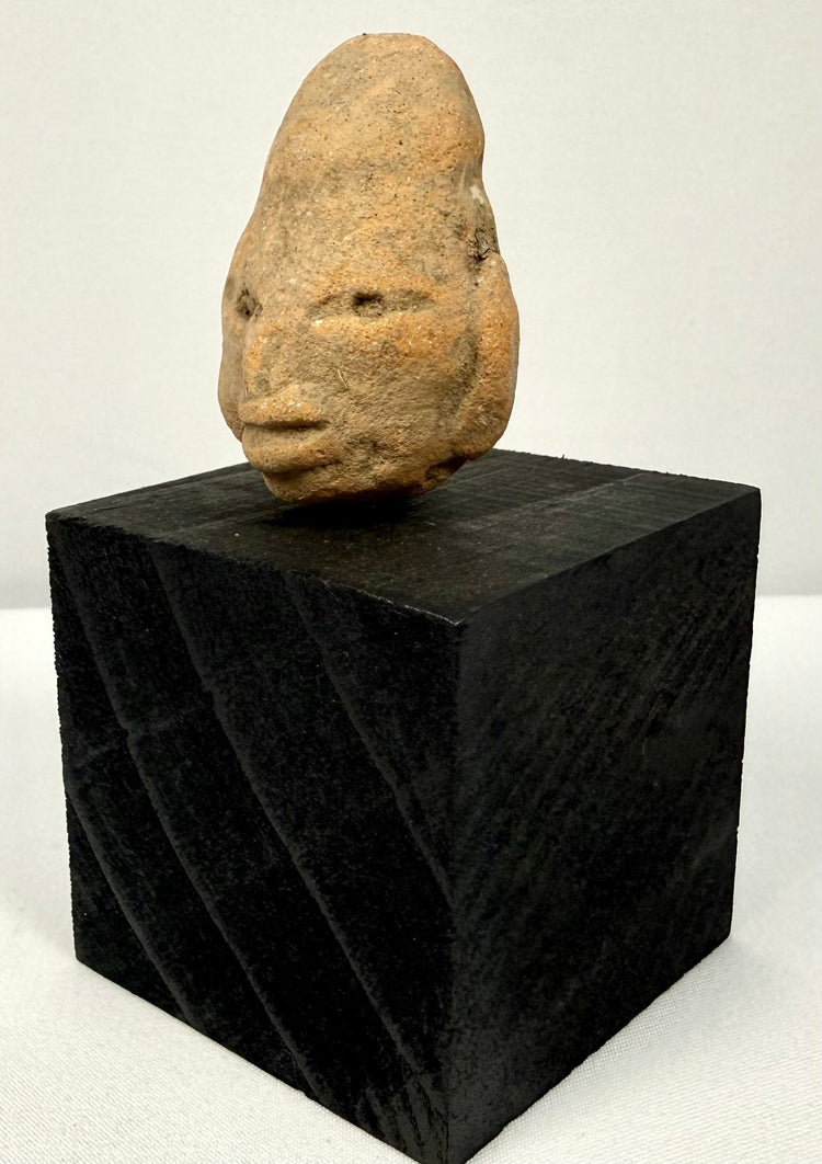 Antique terracotta head sculpture placed on black cubic block to showcase artifact size and form