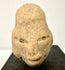 Close-up of ancient terracotta face emphasizing granular clay texture, hollow eye sockets, and defined nose