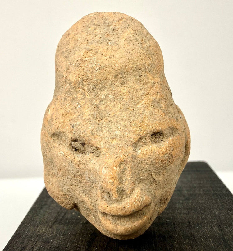 Close-up of ancient terracotta face emphasizing granular clay texture, hollow eye sockets, and defined nose