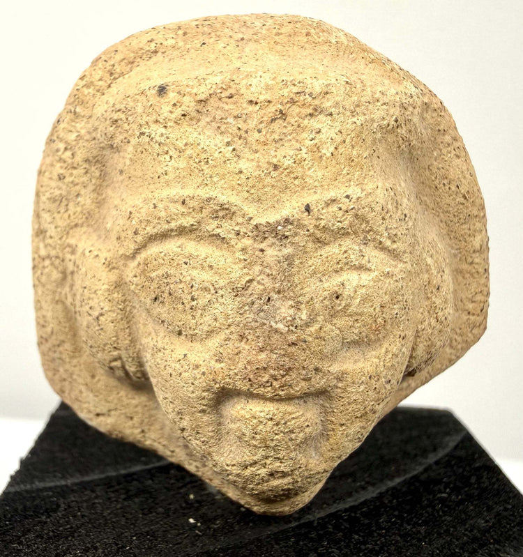 Angled view of ceramic artifact emphasizing grainy material texture and carved eyes