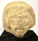 Angled view of ceramic artifact emphasizing grainy material texture and carved eyes
