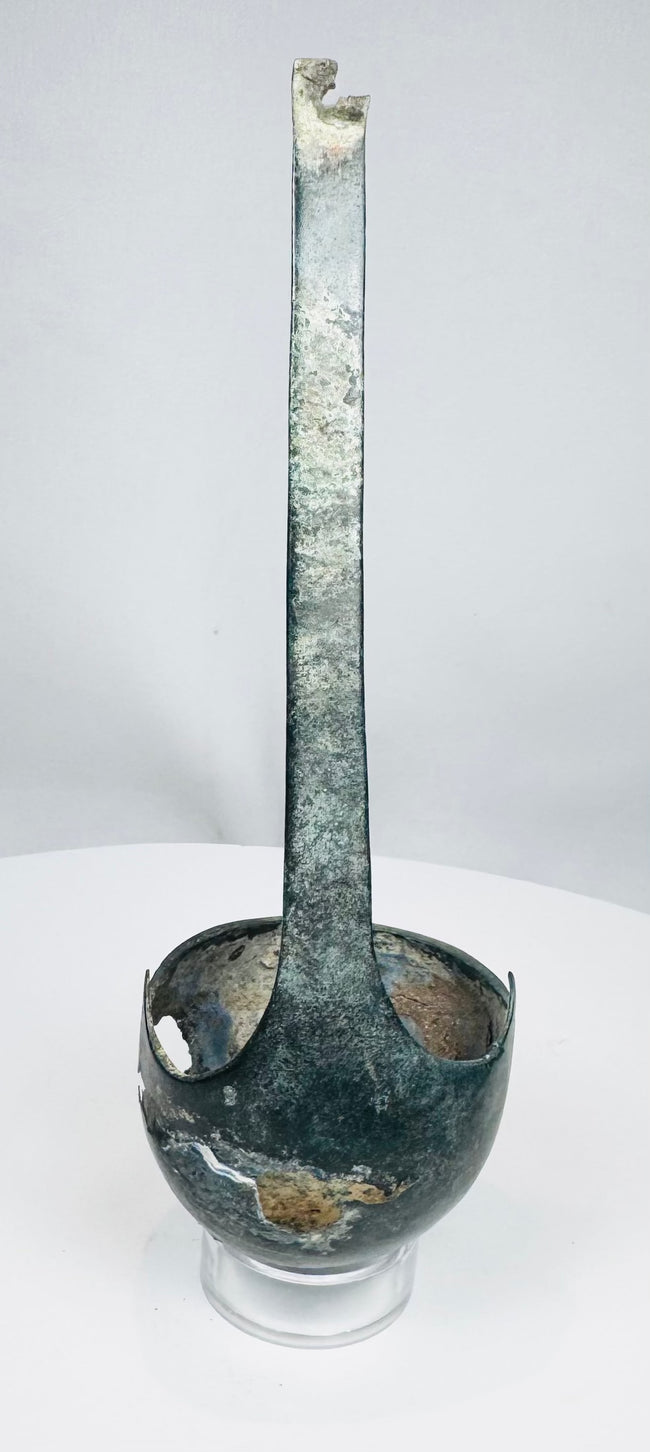 Side view of ancient bronze ladle showing long slightly curved handle