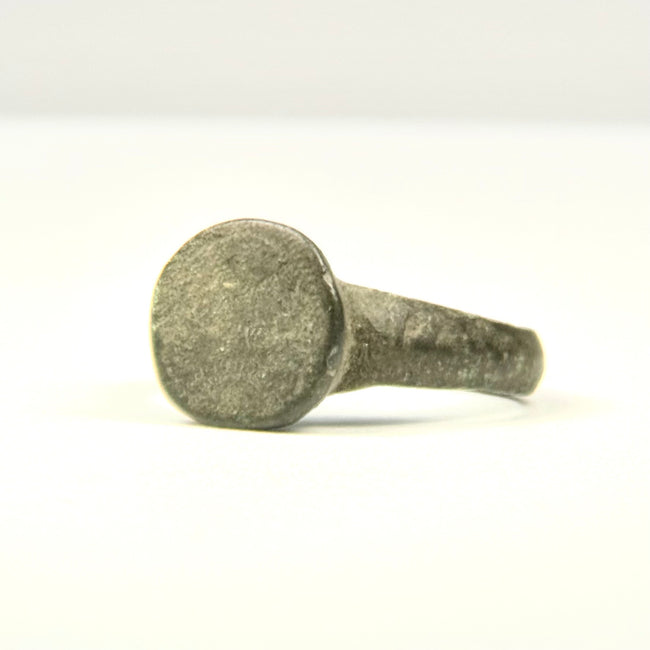 Rear view of ancient bronze ring showing intact hoop, mineral deposits, and localized reddish-brown oxidation