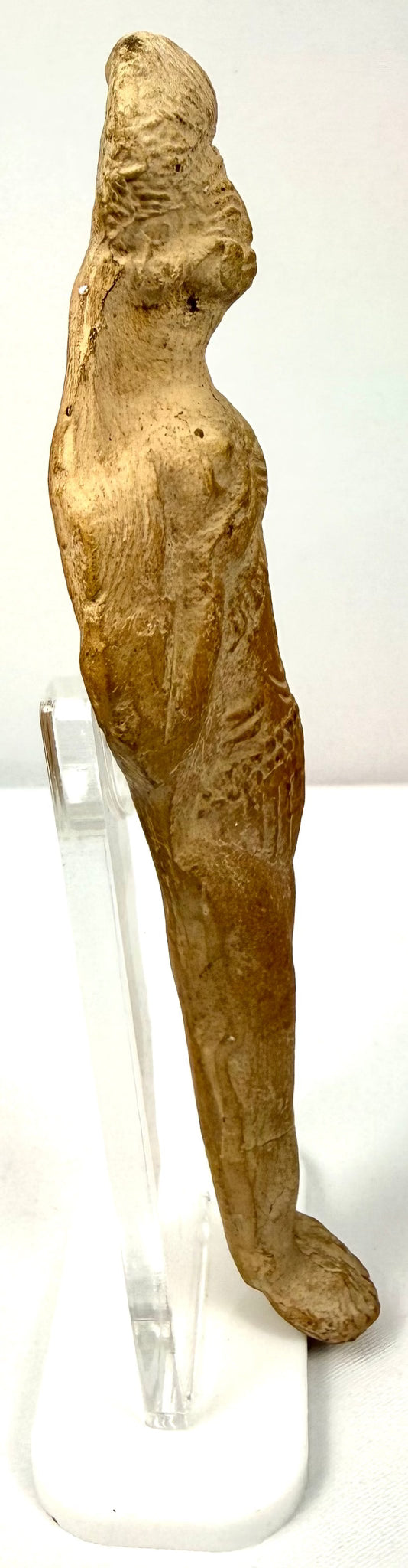 Side profile of beige terracotta figurine showing elongated form and convex back