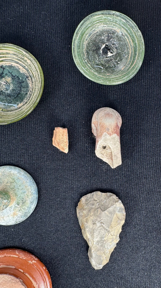 Worked grey stone implement displayed with Roman and Near Eastern archaeological fragments