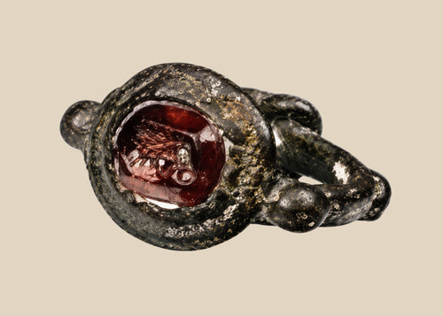 Ancient silver ring from the Eastern Mediterranean or Near East, Late Roman to Early Byzantine period (circa 300–600 CE), featuring a deep red garnet intaglio engraved with symbolic imagery, flanked by decorative silver nodes, preserving its historical elegance and craftsmanship.