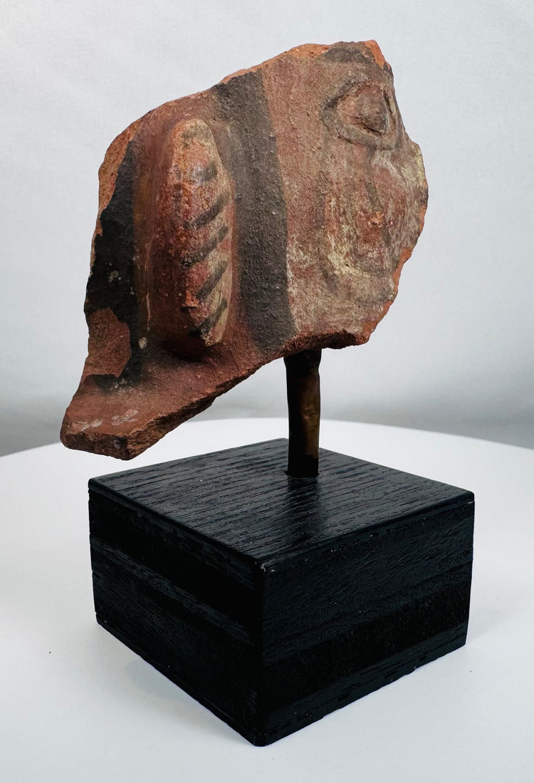 Ancient ceramic figural fragment with preserved facial details and decorative ear ornament on display stand