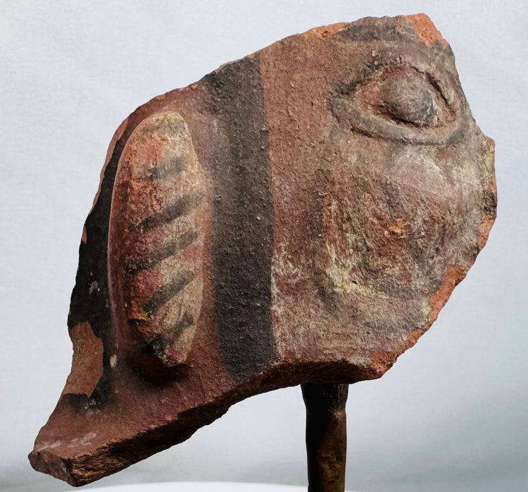 Terracotta face fragment featuring almond-shaped eye and circular earspool with traces of black pigment