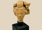 Ancient terracotta head fragment from the Greco-Roman world, circa 4th–1st Century BCE, showing naturalistic facial features and elaborate hairstyle, mounted on a modern black display base, Hellenistic and classical artistic style.