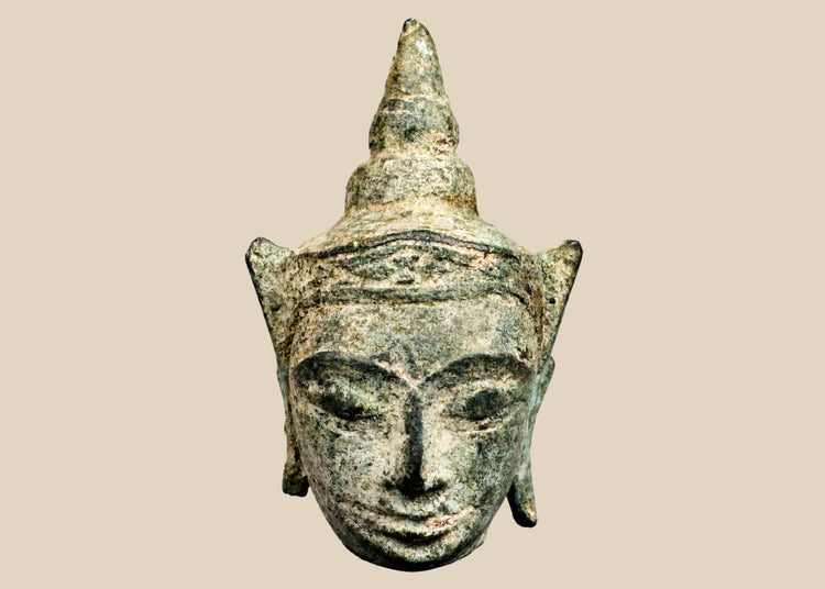 Small antique Southeast Asian bronze Buddha head, likely from Thailand or Cambodia, 16th–17th Century CE. Features serene expression, elongated earlobes, pointed ushnisha, and natural green patina. Originally part of a larger statue, serving as a devotional object reflecting Buddhist spiritual symbolism, artistry, and enlightenment.