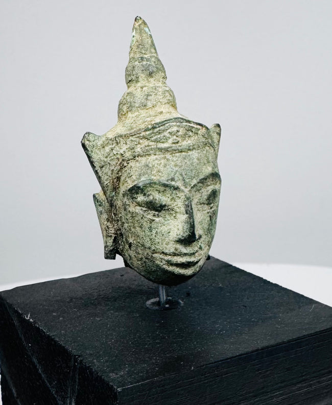 Antique Southeast Asian Buddha head with pointed topknot, tranquil expression, and weathered bronze patina