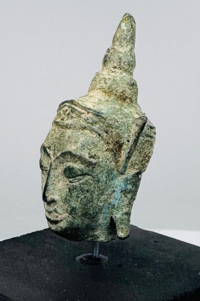 Southeast Asian Buddhist bronze artifact with serene expression, green patina, and symbolic ushnisha