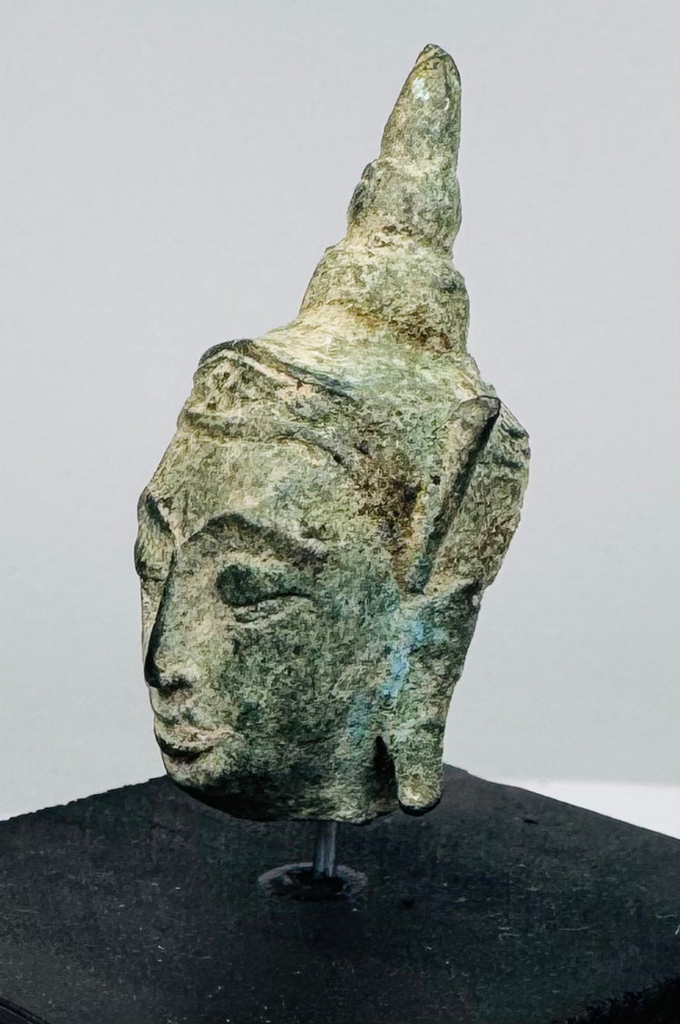 Southeast Asian Buddhist bronze artifact with serene expression, green patina, and symbolic ushnisha