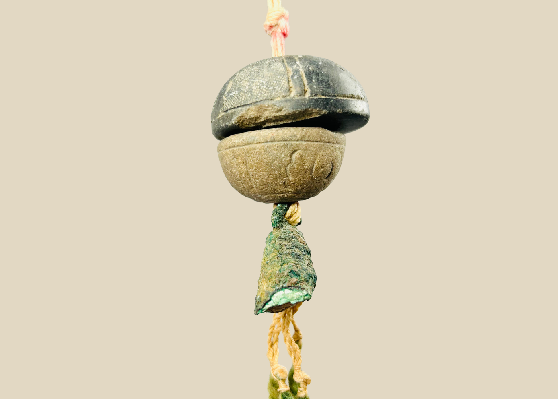 Ancient bronze bell pendant suspended on original fiber cord — full front view showing patina and form