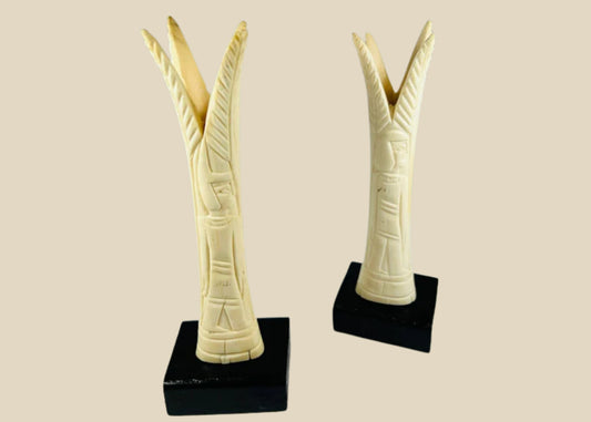 Pair of carved Egyptian ivory sistrum handles on black display bases, featuring stylized figures and decorative motifs, dating to the Third Intermediate Period, circa 1070–664 BCE.