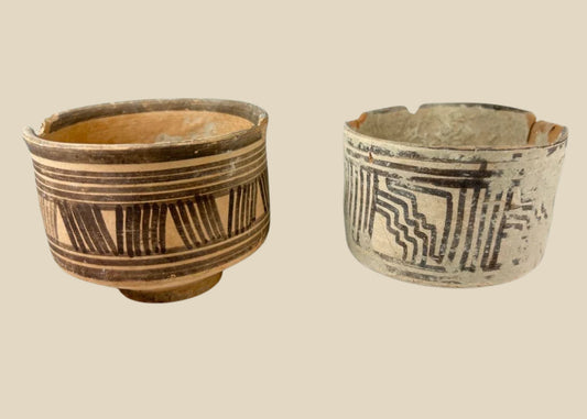 Pair of ancient Harappan terracotta pottery vessels from the Indus Valley Civilization, decorated with bold black geometric linear and zigzag motifs; hand-crafted, wide-bodied bowls with rimmed edges, dating circa 2600–1900 BCE, showing surface wear, minor chipping, and aged earthen patina consistent with archaeological finds.