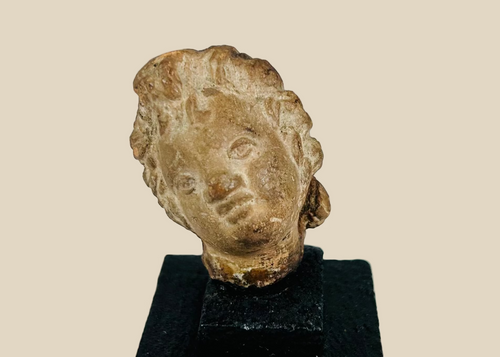 Ancient terracotta or stone head fragment, circa 1st millennium BCE–CE, likely Greek, Roman, or Near Eastern, stylized facial features with warm patina, mounted on display base