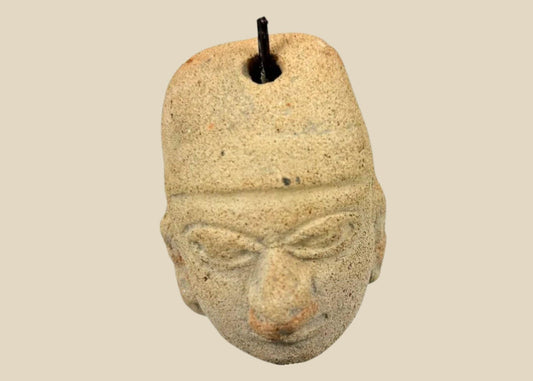 Terracotta pendant head with angular headdress, incised almond-shaped eyes, furrowed brow, and pronounced nose and lips; drilled suspension hole through top; mounted on a museum-style stand; West Mexico (Colima/Nayarit) or Veracruz, circa 300 BCE–300 CE.