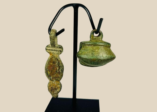 Ancient Roman bronze artifacts, circa 1st–4th century CE, including a patinated pendant and small ritual bell displayed on a custom stand.