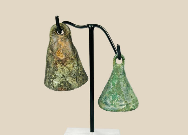 Pair of Ancient Roman cast bronze bells, 1st–4th century CE, conical form with suspension loops, green patina, and mounted display stand.
