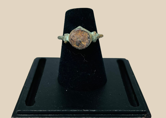 Ancient bronze ring with engraved bezel displayed on a black jewelry stand