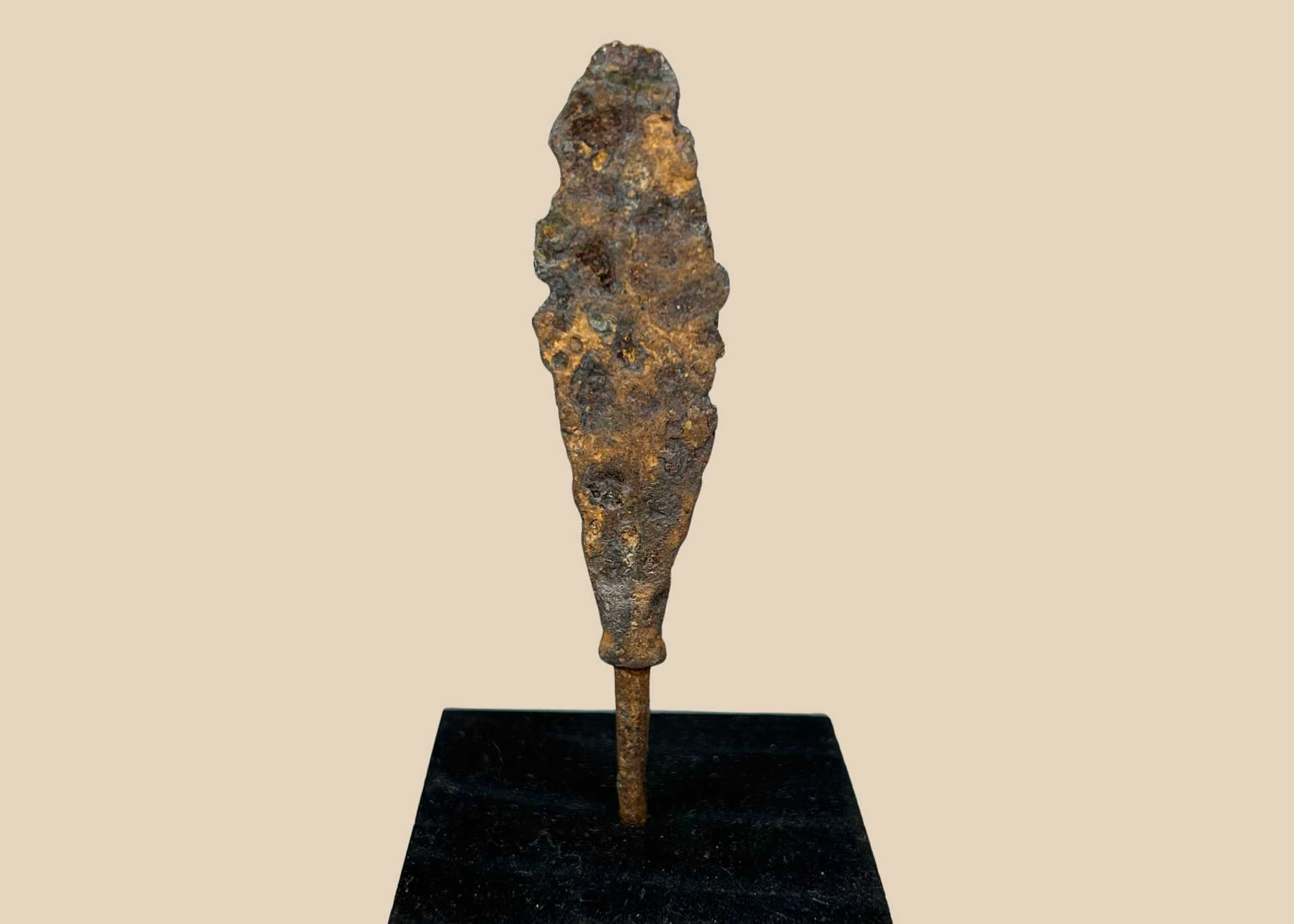Ancient iron arrowhead relic mounted on black display base, front view.