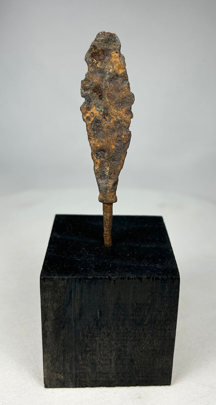 Ancient iron arrowhead relic mounted on black display base, front view.