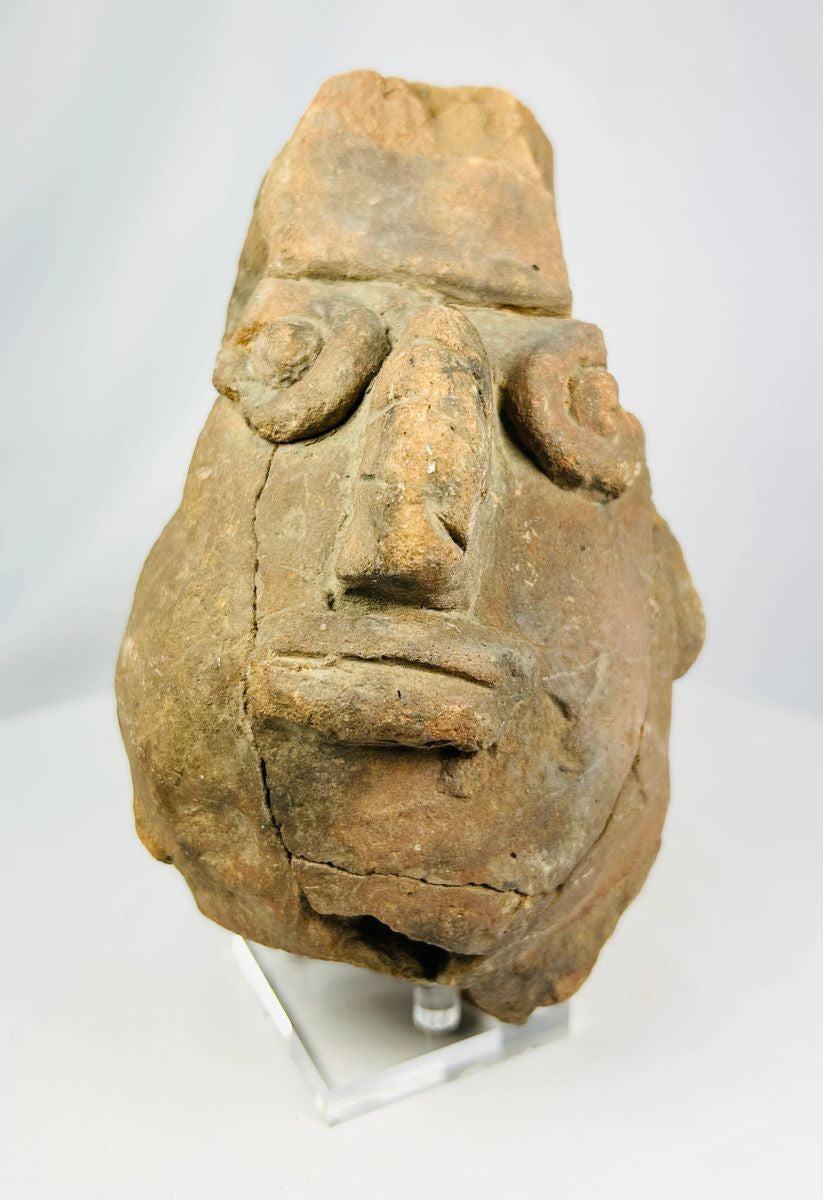 Pre-Columbian anthropomorphic spouted jar from the Valdivia–Chorrera culture, Ecuador, shaped as a stylized human head with large circular eyes, broad nose, and pronounced lips; hand-molded terracotta with earthy patina, ritual vessel dating to early Andean traditions, showing surface wear and archaeological age cracks.