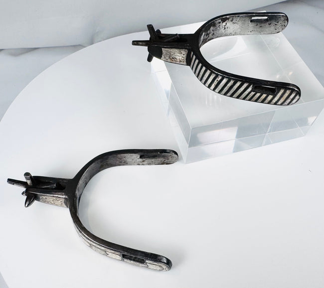 Decorated steel cowboy spurs with silver overlays, strap slots, and aged surface