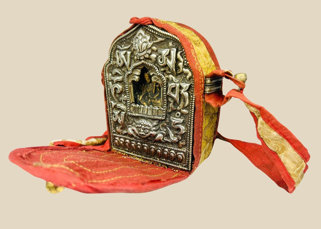 18th–19th century Tibetan Gau shrine, silvered copper alloy with repoussé seated Buddha, gilt backing plate, and original red fabric strap, portable Himalayan Buddhist amulet box