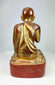 Close-up of red lacquer pedestal supporting the Burmese monk statue, showing aged texture and hand-carved form.