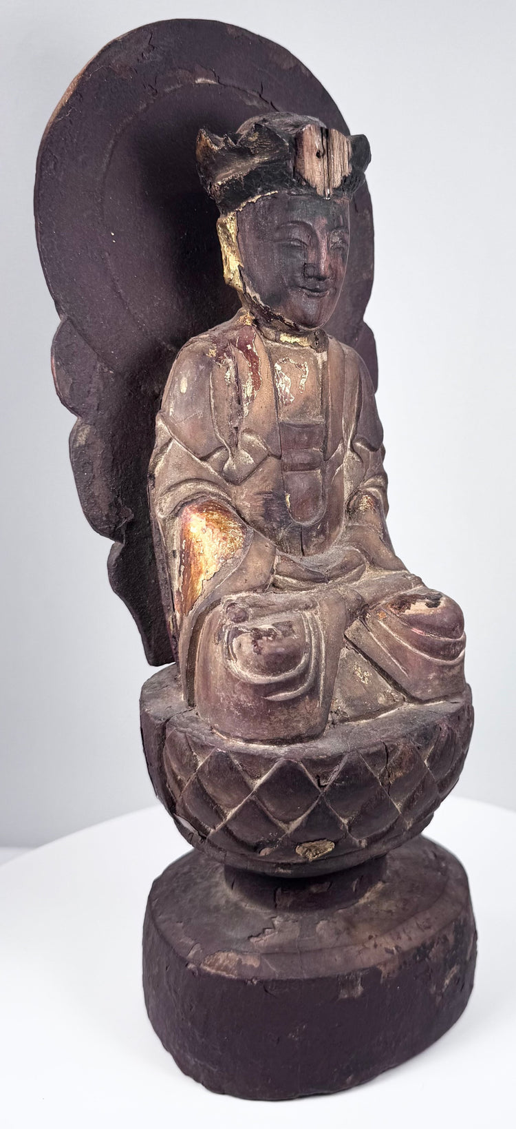 Aged circular wooden pedestal supporting the Guanyin statue with cinnabar-red pigment, cracks and historic surface losses
