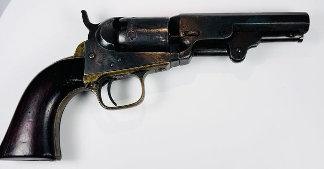 Antique Colt Model 1849 Pocket Revolver with an exposed hammer, worn steel cylinder, and warm-toned brass trigger guard.