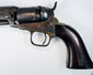 Colt Model 1849 Pocket Revolver detail showing the cylinder and exposed hammer above the brass trigger guard and walnut grip.