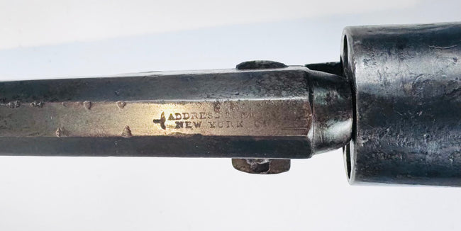 Close-up of faint stamped lettering and surface wear on the Colt Model 1849 Pocket Revolver’s octagonal steel barrel.