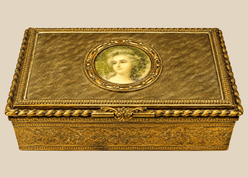 Antique gold decorative box featuring a painted portrait miniature of a woman displayed on a beige background.