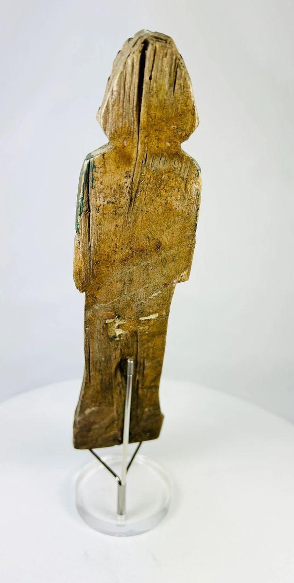 Rear view of hand-carved wooden figurine displaying age-related wear and carving details.