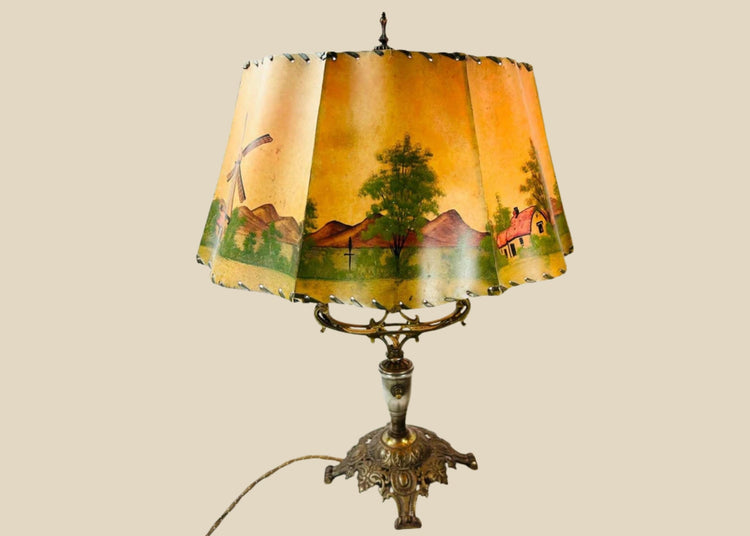 Antique Art Nouveau table lamp, circa 1920s, with ornate cast metal base and original hand-painted parchment shade depicting cottages, windmills, and trees, a decorative European lighting piece with warm pastoral charm.