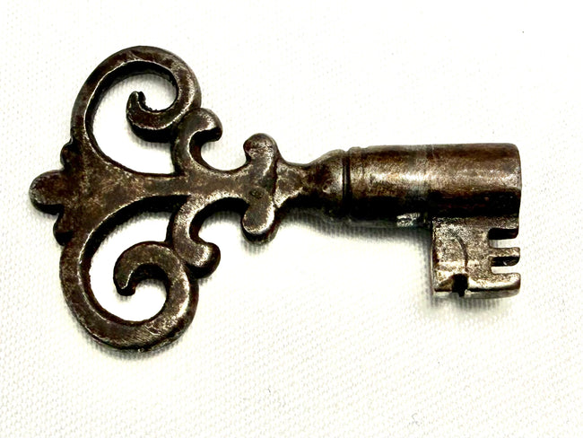 Close-up of ornate hand-forged iron skeleton key with intricate scrollwork bow and bitted end