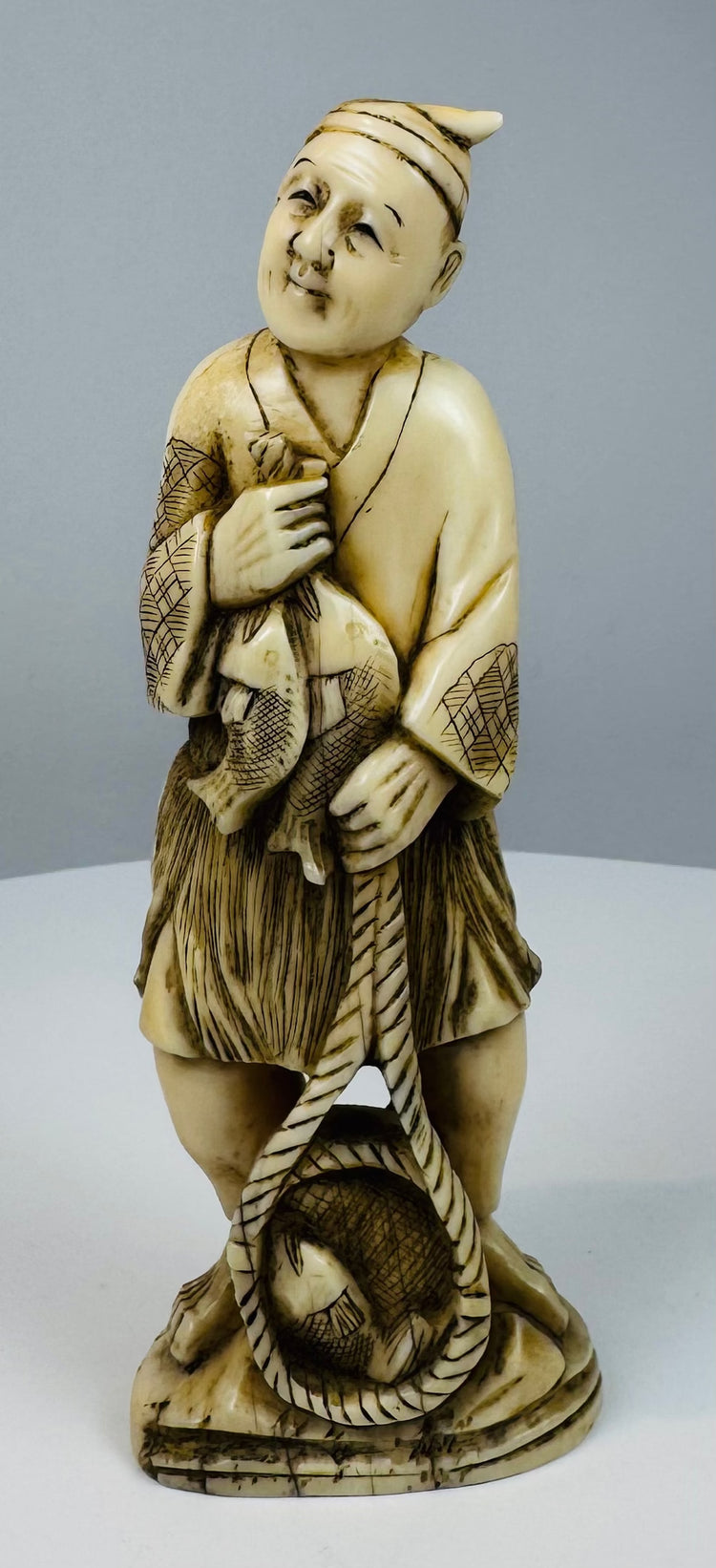 Three-quarter view of an antique Japanese fisherman figure with carved fish and rope
